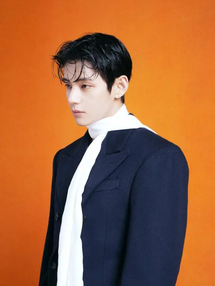 BTS’s V with wet black hair wearing a dark coat and a white scarf, posed against a vibrant orange background.
