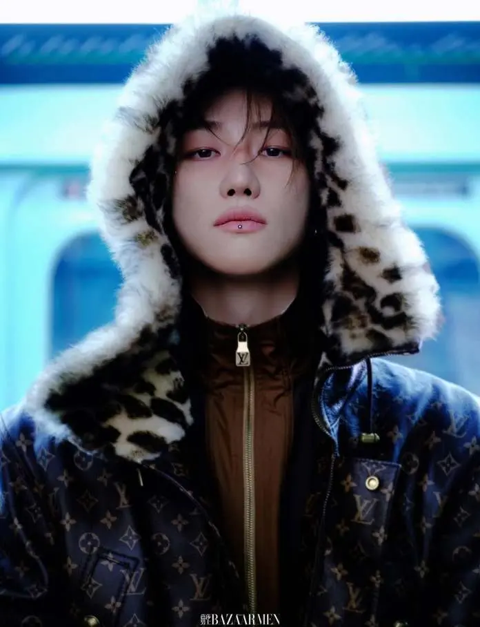 The8 wearing a leopard-print hooded coat stands confidently, with a piercing gaze. The background features a subway interior.