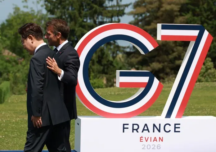Presidents of South Korea and France walk past a large 'G7' sign, featuring the colors of the French flag, set in a green outdoor area during a summit.
