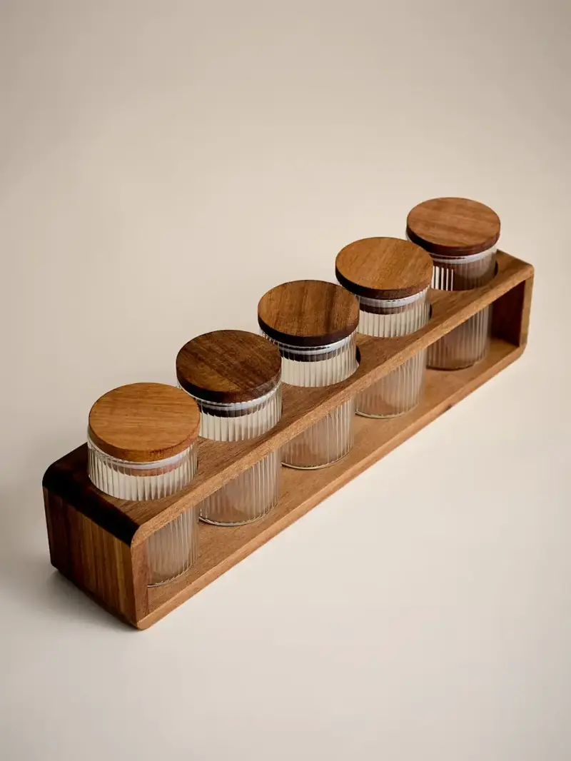 A wooden holder with five ribbed glass spice jars with lids from M&S