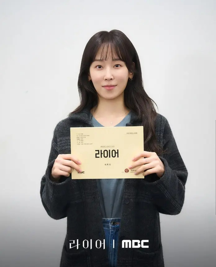 Seo Hyun-jin holding a script titled '라이어' in front of a plain background, wearing a black cardigan and a gray top.