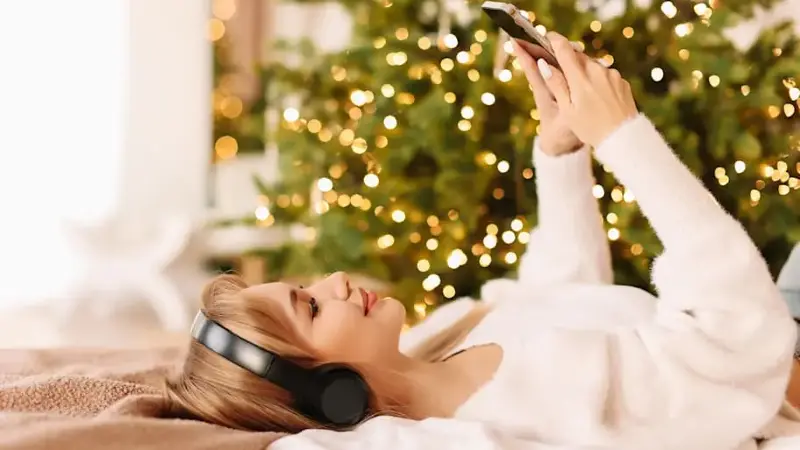 A girl is lying on the bed listening to Christmas music with headphones