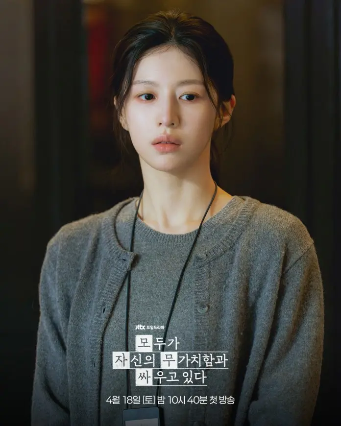 Go Youn-jung with long dark hair wearing a gray cardigan, looking contemplative against a blurred background.