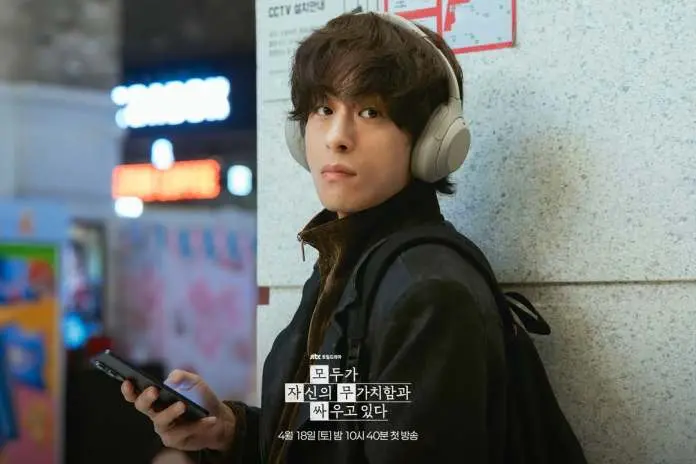 Koo Kyo-hwan wearing headphones, looking thoughtfully at their phone while leaning against a wall in a busy urban setting.