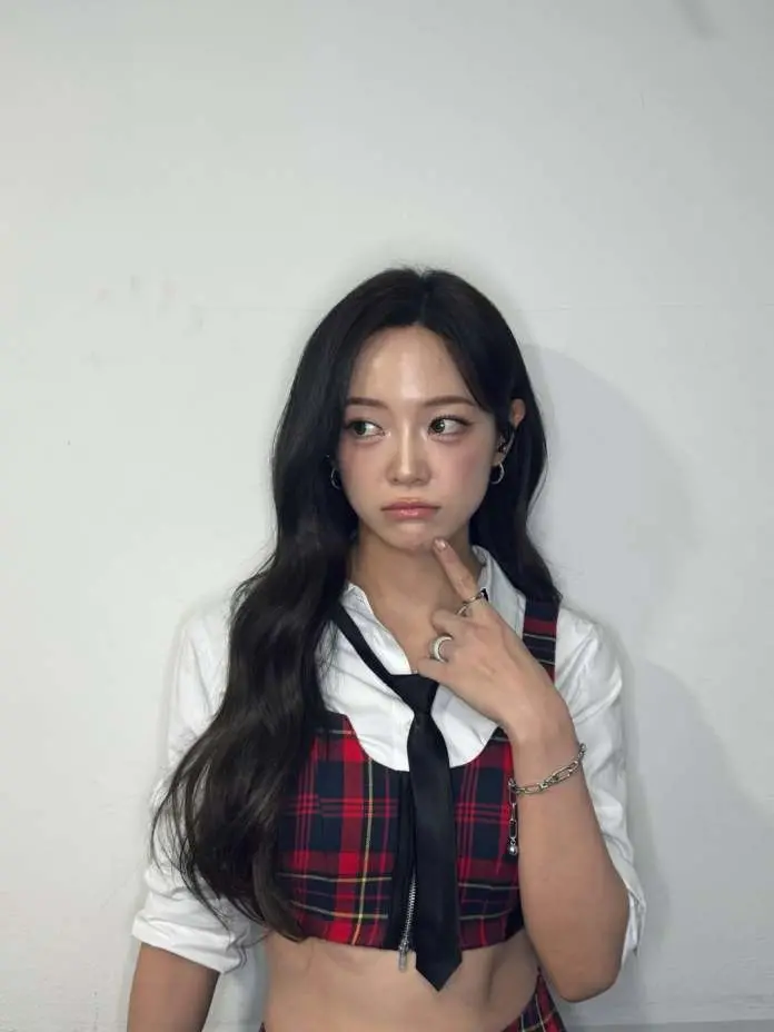 Kim Sejeong with long dark hair, wearing a red plaid crop top with a white shirt underneath and a black tie, poses with a thoughtful expression against a plain white background.