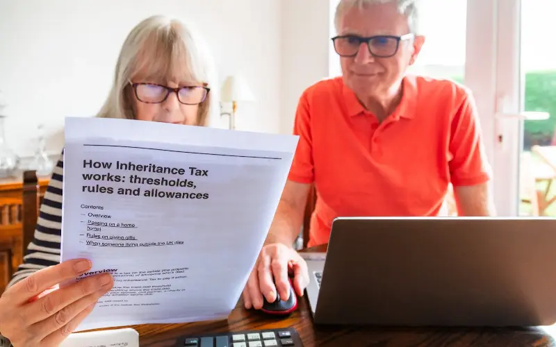A senior married couple in their 70s study inheritance tax documents sitting down in their living room at home.
