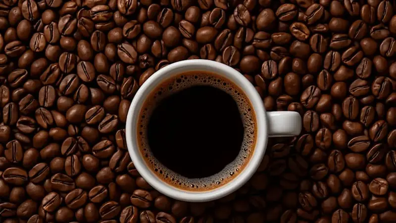 White cup of black coffee on coffee beans background, top view
