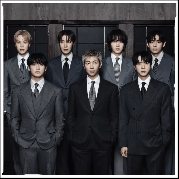 A group of eight men dressed in stylish suits, standing in two rows against a dark background.