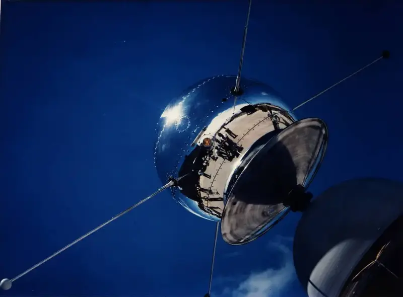 A reflective silver Vanguard satellite with long aerials against a blue sky