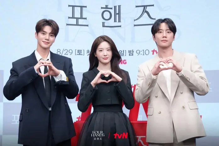 Song Kang Jang Gyuri and Lee Jun-young forming heart shapes with their hands, posing at a promotional event for the show 'Four Hands'.