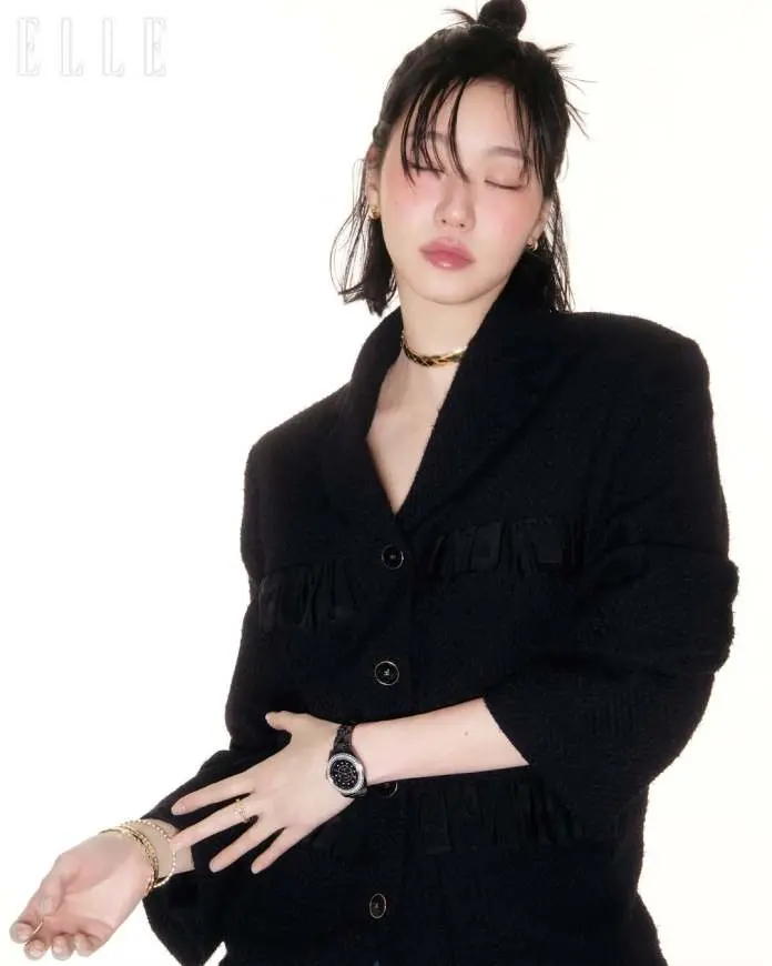 Kim Go-eun wearing a black oversized blazer, adorned with jewelry including earrings and a bracelet, poses with her eyes closed against a light background.