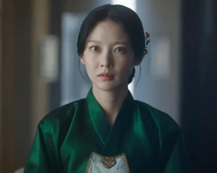 Gong Seung-yeon wearing a traditional green hanbok, with a solemn expression and styled hair adorned with accessories.