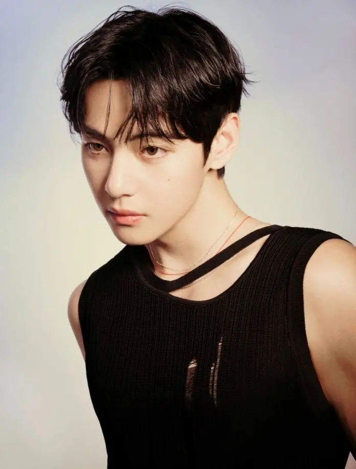 A close-up portrait of V with dark hair and wearing a sleeveless black top, tilted slightly to one side with a neutral expression.