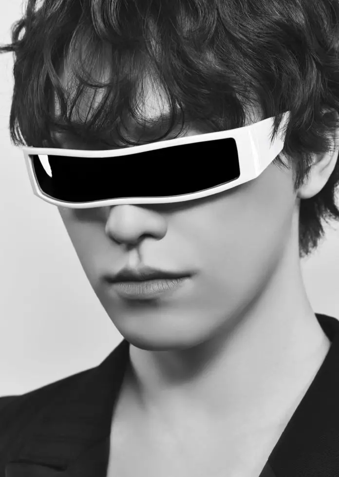 Close-up portrait of Dino with curly hair wearing futuristic white sunglasses, against a plain background.