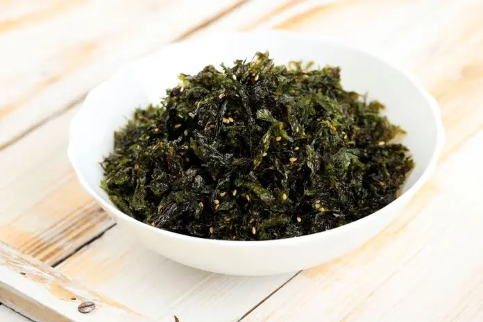 A bowl of crispy seaweed snacks garnished with sesame seeds, placed on a wooden surface.