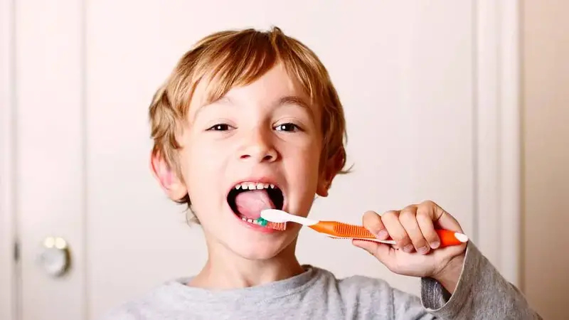 Young boy brushing his teeth with orange toothbrush 