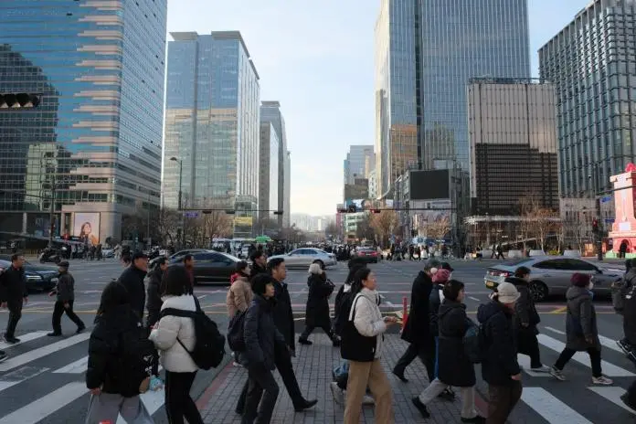 Busy city street in an urban area with pedestrians crossing at a crosswalk, surrounded by tall skyscrapers and vehicles on the road.