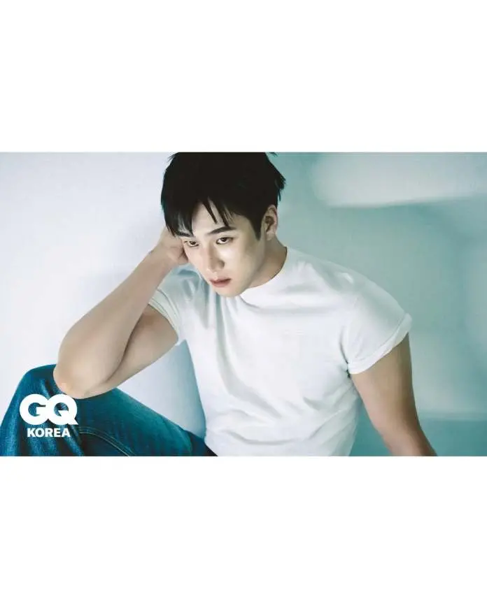 Ahn Bo-hyun in a white t-shirt sits against a light background, resting his head on his hand with a thoughtful expression. He is wearing blue jeans and has dark, styled hair.