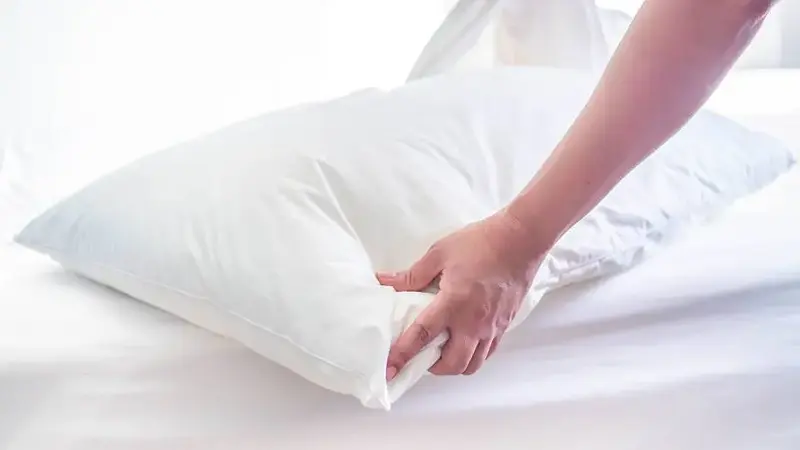White pillow on the bed in the bedroom with woman 's hand who are making the room.