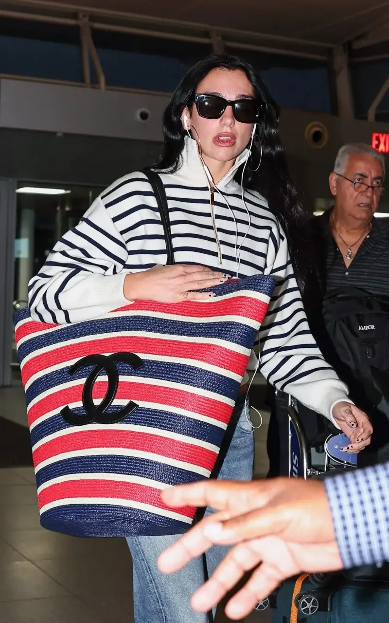 Dua Lipa was seen carrying a striped wicker beach bag from Chanel as she embarked on her latest summer getaway - AKGS