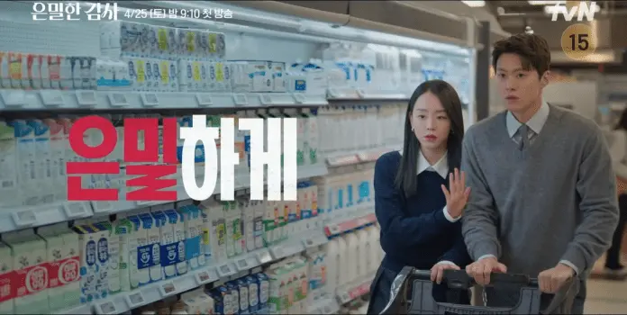 Shin Hye Sun in a dark sweater and Gong Myung  in a light sweater are shopping in a supermarket aisle filled with dairy products. Shin Hye Sun is gesturing towards something while Gong Myung  looks concerned.