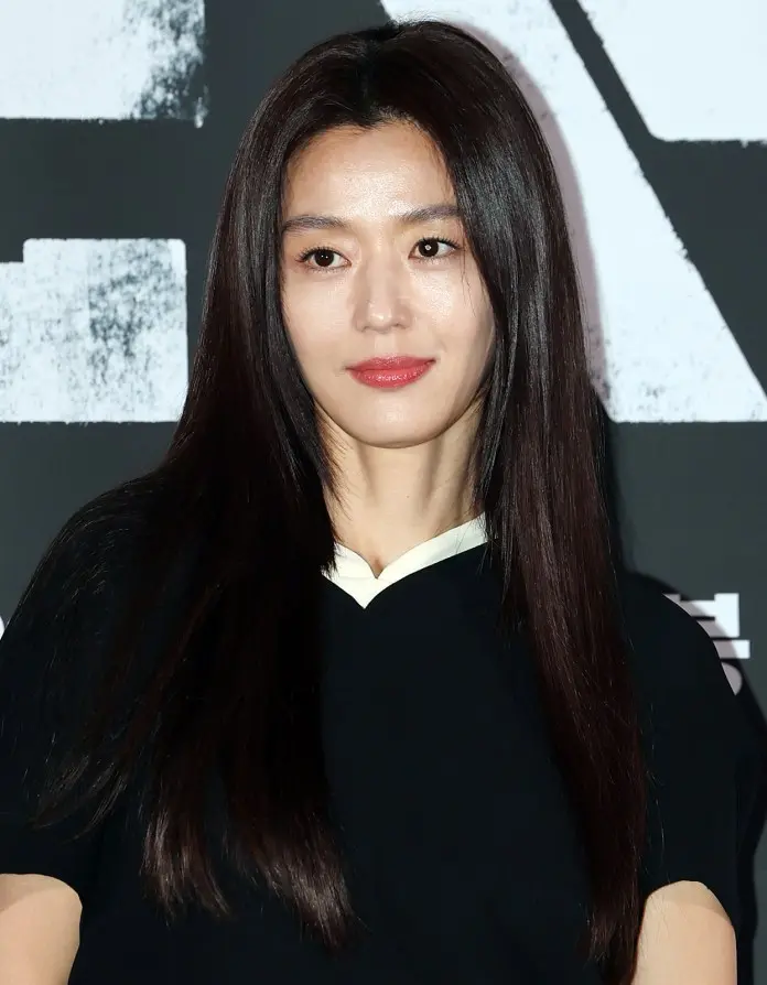 Jun Ji-hyun wearing a black dress with a white collar, posing in front of a textured background.