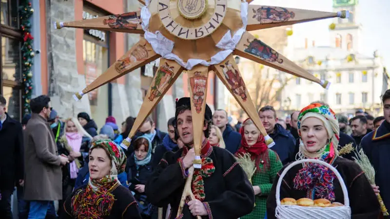 Ukrainians sing Christmas carols as they carry a huge...