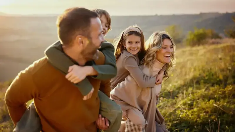 Happy parents piggybacking their kids in autumn day.