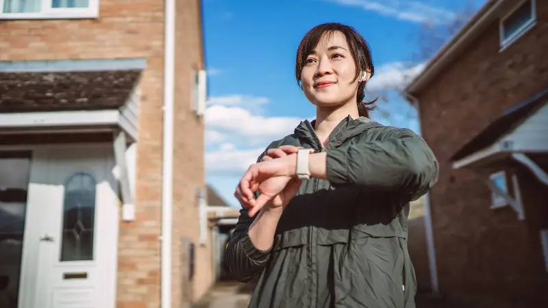 Woman outside a house pressing buttons on her smartwatch