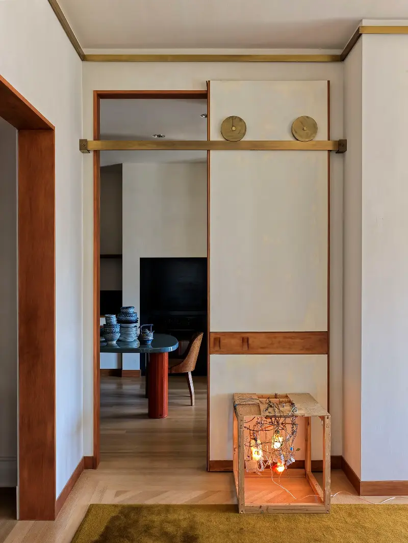 Through the gap, the kitchen appears in pieces: a stack of bowls, a red column, the curve of a chair back.Chris Mottalini. Design: Crina Arghirescu Rogard.