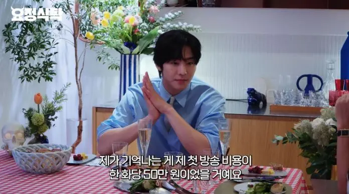 Ahn Hyo-seop sitting at a dining table with a blue shirt, hands clasped, surrounded by food and decorative items.