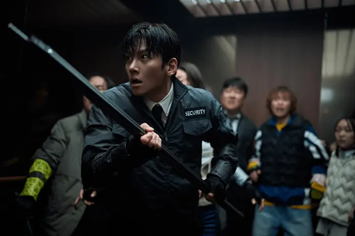 A tense moment in an elevator showing a Ji Chang Wook holding a baton, looking alarmed, surrounded by a group of frightened people.