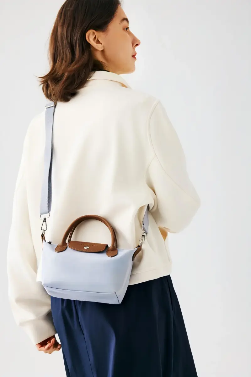 Light blue Skechers shoulder bag with brown leather handles worn crossbody over a cream jacket and navy skirt