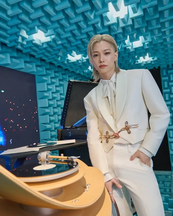 Felix wearing a stylish white suit stands beside a turntable in a soundproof room decorated with blue acoustic panels.