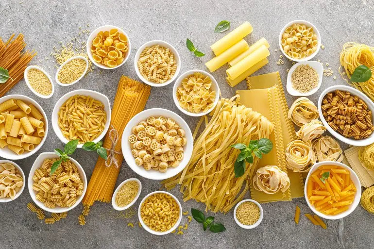 Pasta. Various kinds of uncooked pasta and noodles over stone background, top view with copy space for text. Italian food culinary concept. Collection of different raw pasta on cooking table