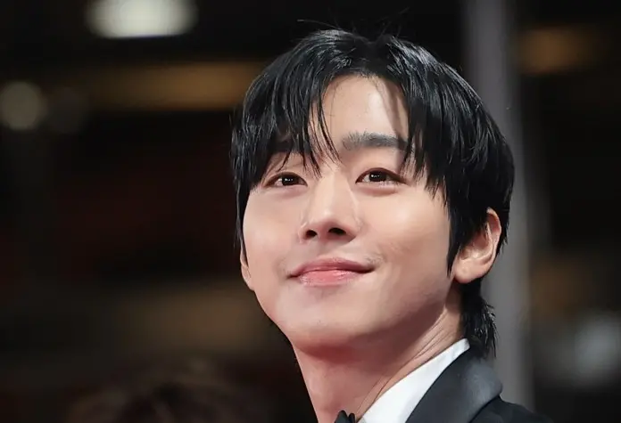 Close-up portrait of a smiling Ahn Hyo-seop with dark hair and a slight smirk, dressed in a formal suit.