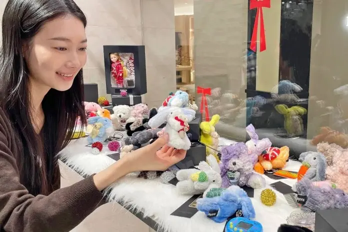 A young woman smiling while holding a stuffed animal, surrounded by various colorful plush toys on a display table.