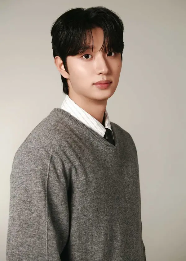 Kim Jaewon with dark hair wearing a gray sweater over a white collared shirt and a black tie, posing against a light background.