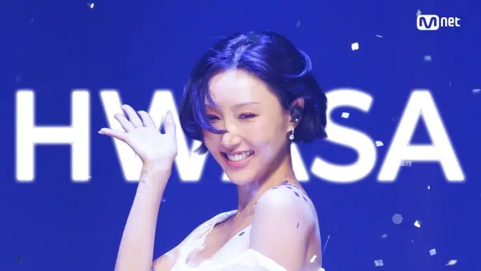 HWASA with short hair wearing a white outfit, waving one hand amidst falling confetti, with the word 'HWASA' displayed in the background.