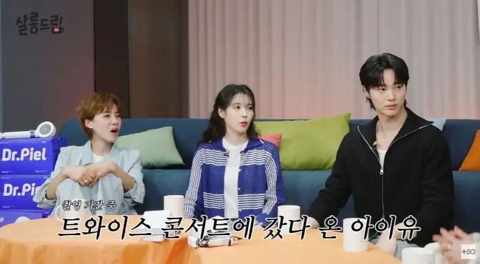 IU and Byeon Woo-seok seated at a table during a filming session, discussing their experience at a TWICE concert. The scene includes IU and Byeon Woo-seok, with various colored cushions in the background.