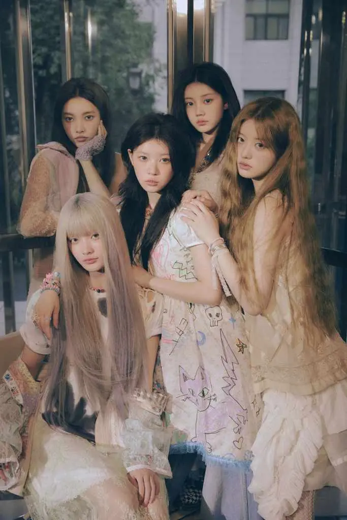 A group of five young women posing together indoors, wearing stylish, pastel-colored outfits and accessories. They are standing in front of large glass windows, with soft lighting highlighting their features.