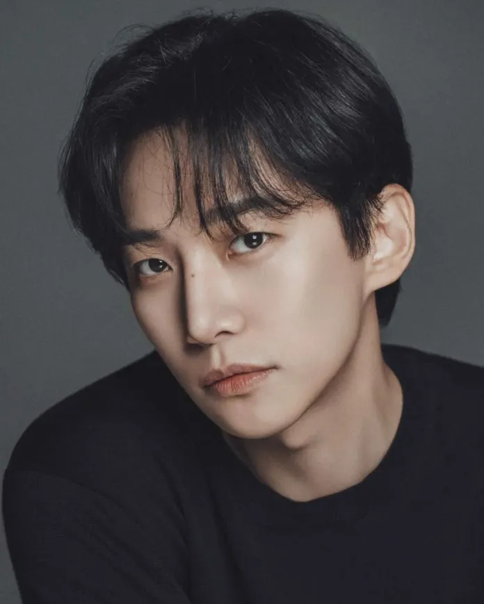 Close-up portrait of Lee Junho with dark hair, wearing a black shirt, against a neutral background, showcasing a thoughtful expression.