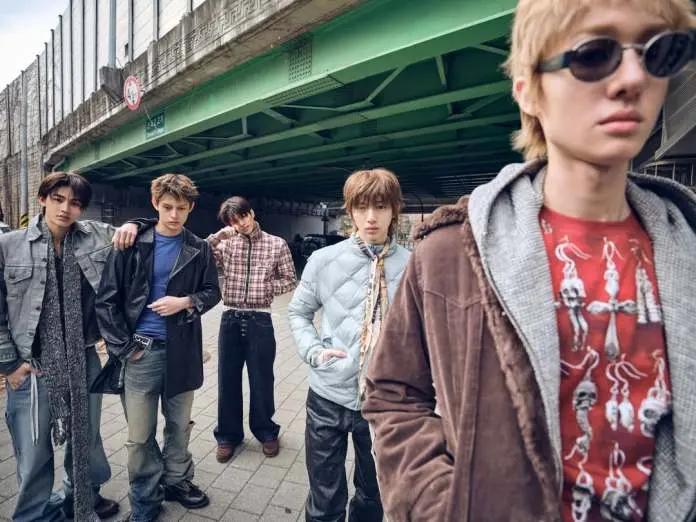 CORTIS members posing under a green bridge in an urban setting, showcasing diverse fashion styles, including leather jackets, plaid shirts, and casual attire.