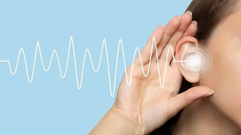 A woman puts her hand to her right ear and listens