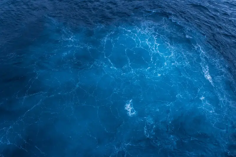 Aerial view of the sunlit ocean surface with swirling patterns.