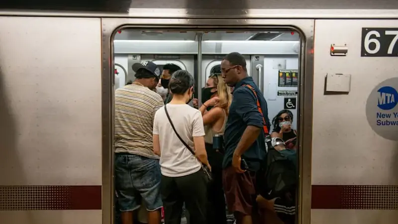 A crowd of people ride a New York City subway car as seen through the open doors.