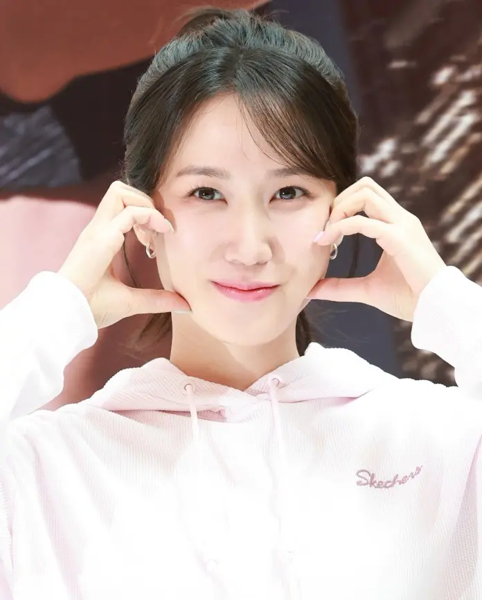 Park Eun-bin a pink hoodie makes a playful gesture with her hands near her face, smiling at the camera.