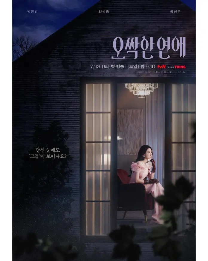 Park Eun-bin in a pink dress sits on a chair by a window, holding a coffee cup, with a dark, moody exterior and illuminated interior.