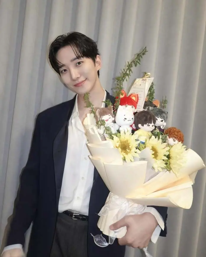 Lee Junho holding a bouquet featuring flowers and small plush toys, smiling with a neutral background.