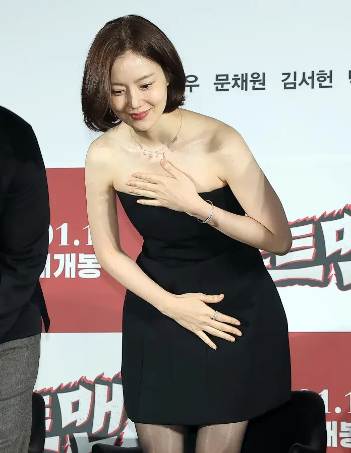 Moon Chae-won in a black sleeveless dress smiling and bowing slightly at a promotional event, with a backdrop featuring text in Korean.